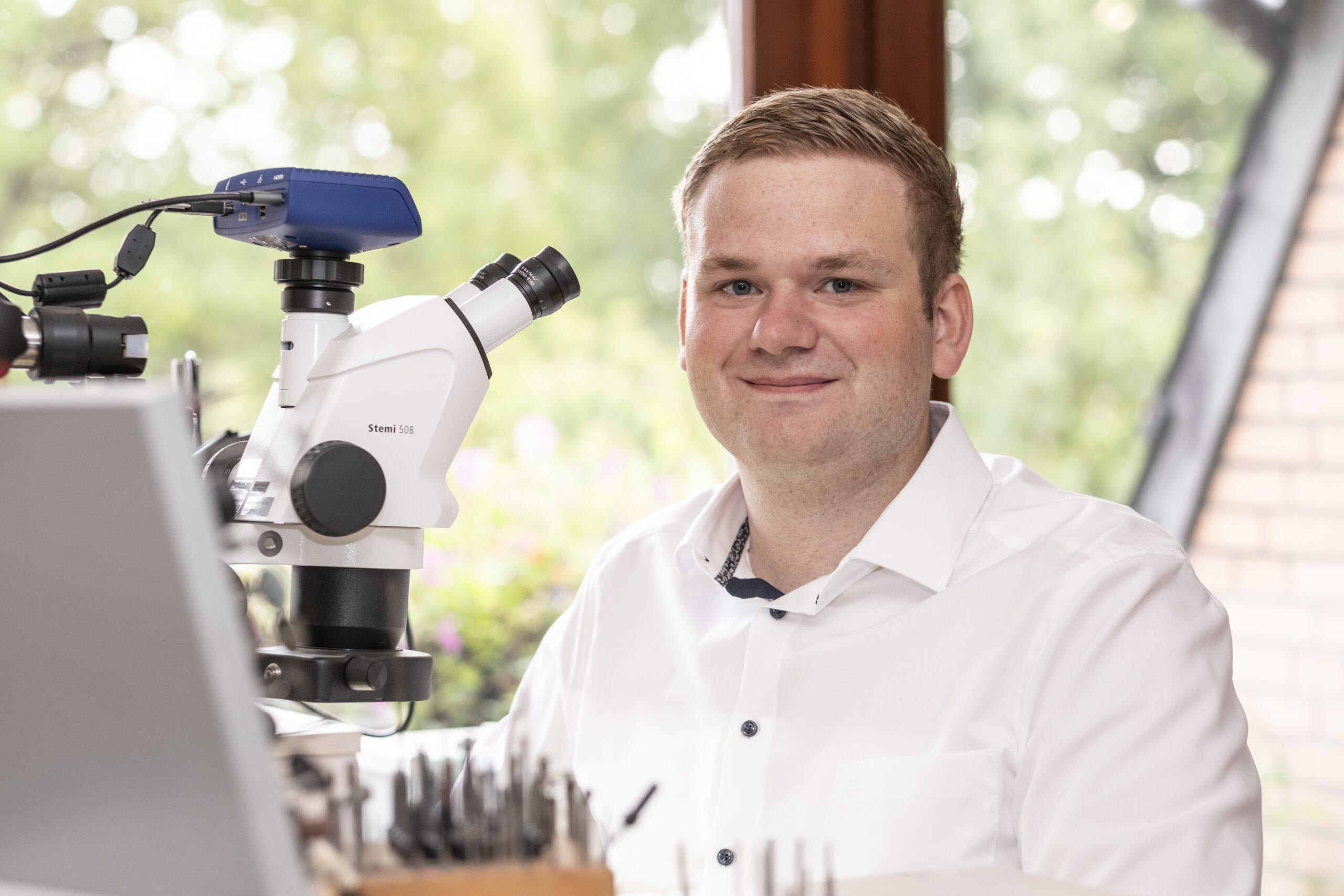 Johannes Segelken sitzt am Mikroskop und lächelt in die Kamera